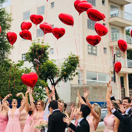 Gruppo di persone che festeggia lanciando in aria palloncini a forma di cuore